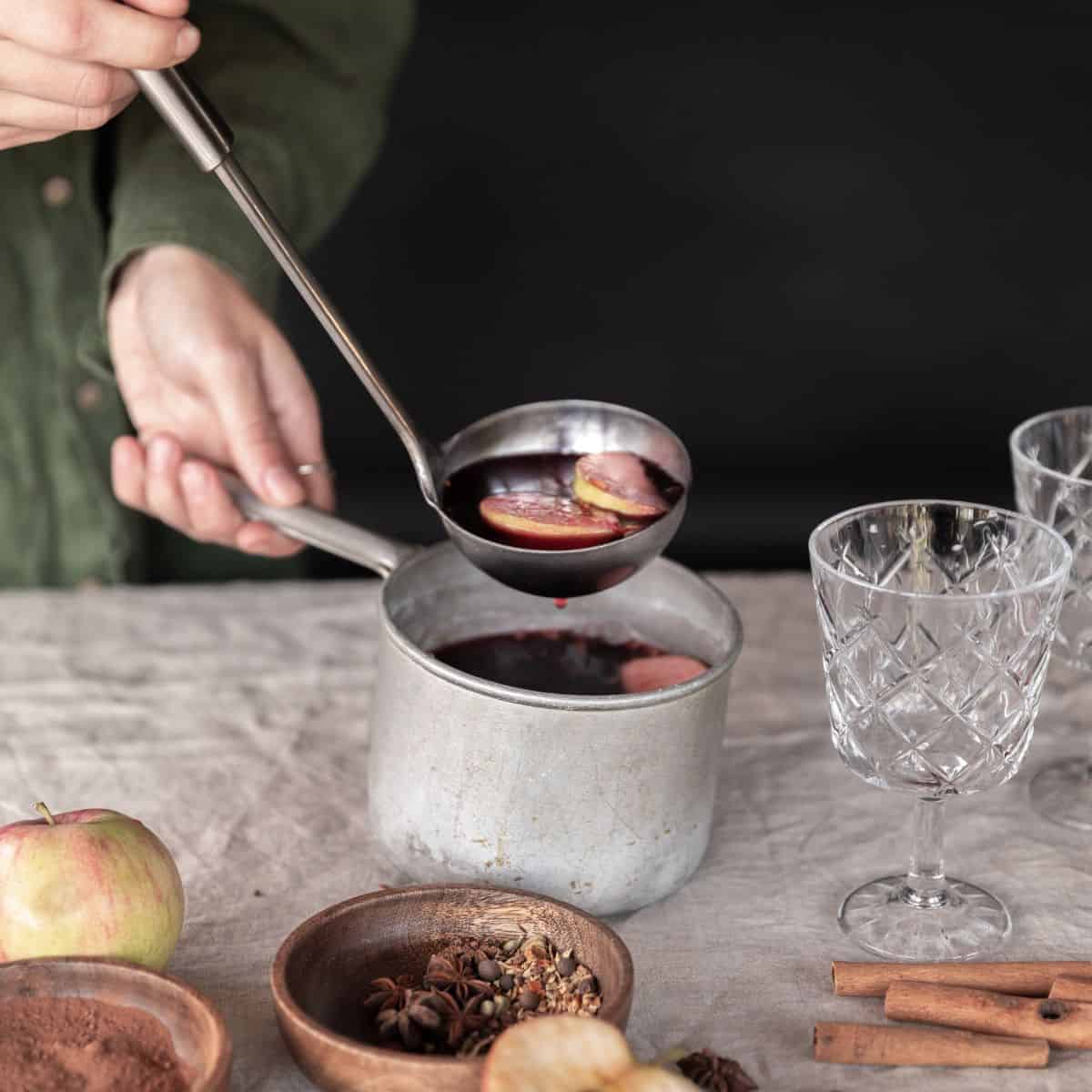 mulled wine in a sauce pan with spices on the side and 2 clear glass cup