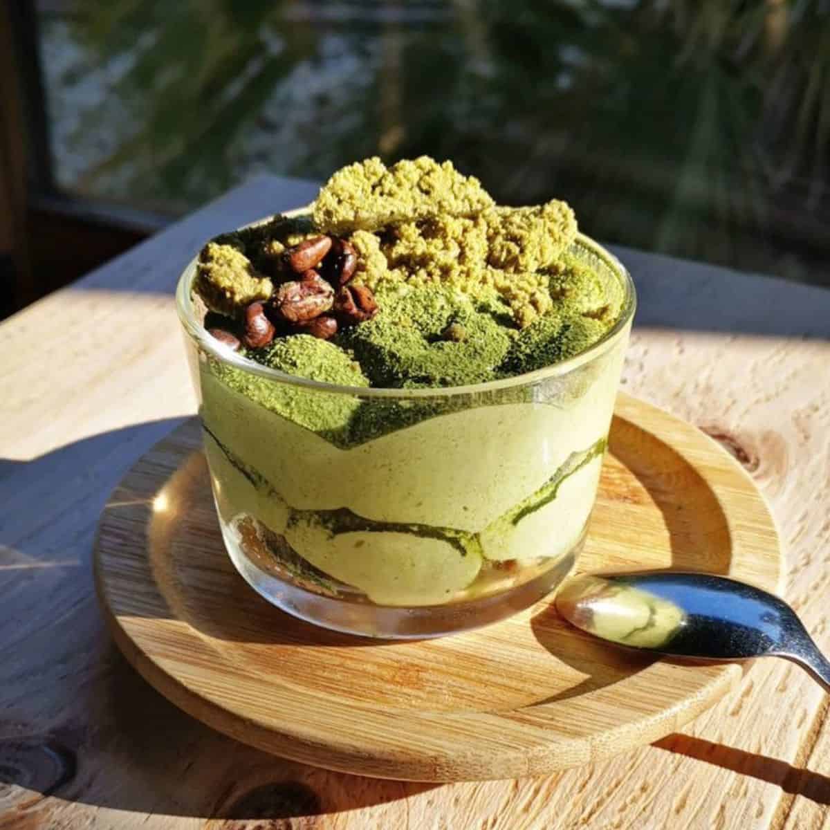 A glass of layered green tea dessert with coffee beans on top.
