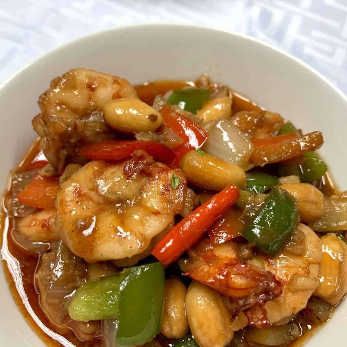 Kung Pao Shrimp served in a white bowl, topped with chilli, peanuts, and bell peppers