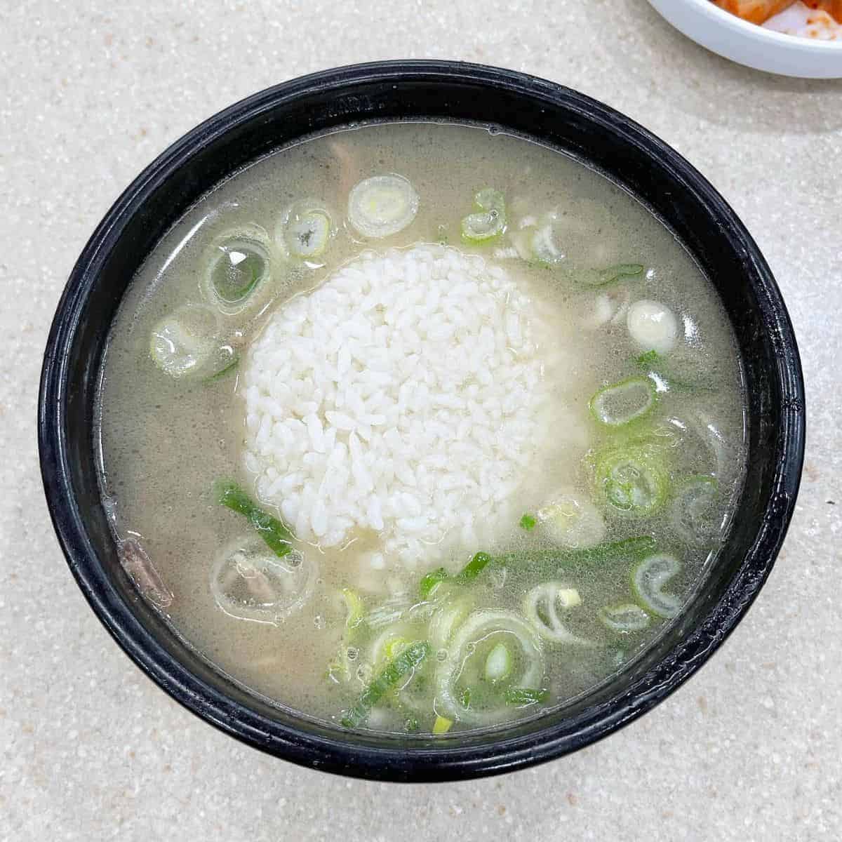 A cup of rice drowned in a hot broth with sliced scallions
