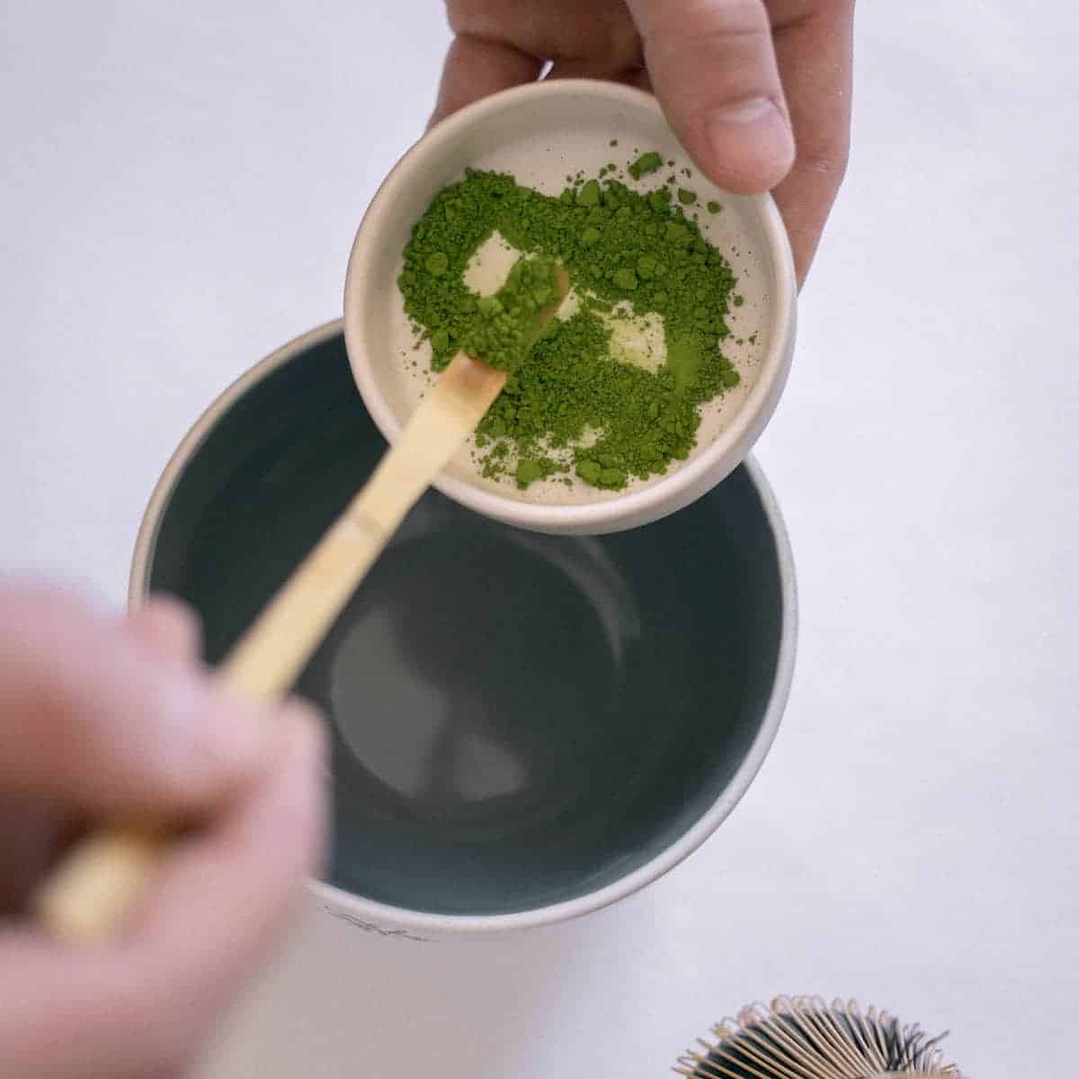 A hand holding a small white bowl of green tea powder