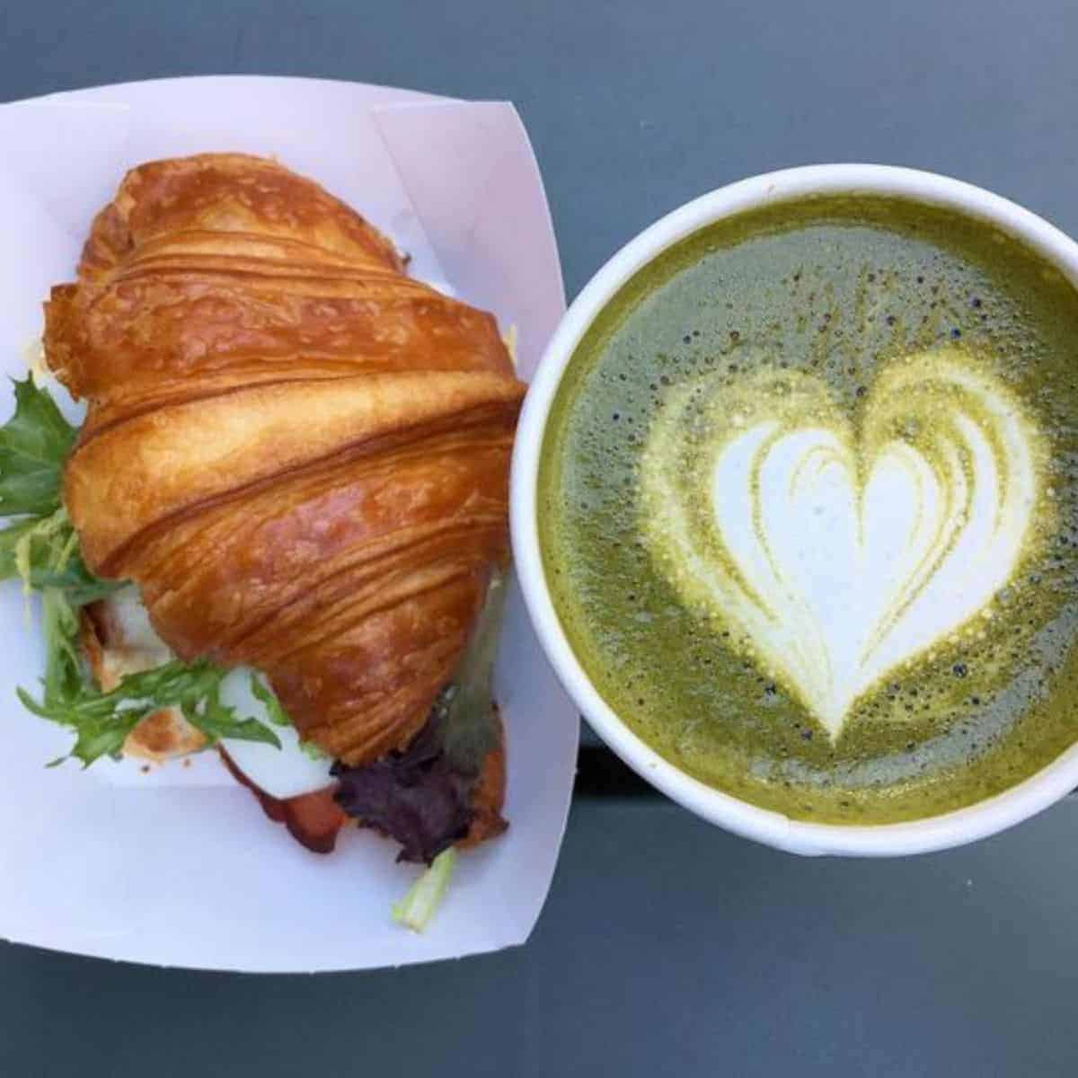 A hot beverage paired with a croissant with green garnishes