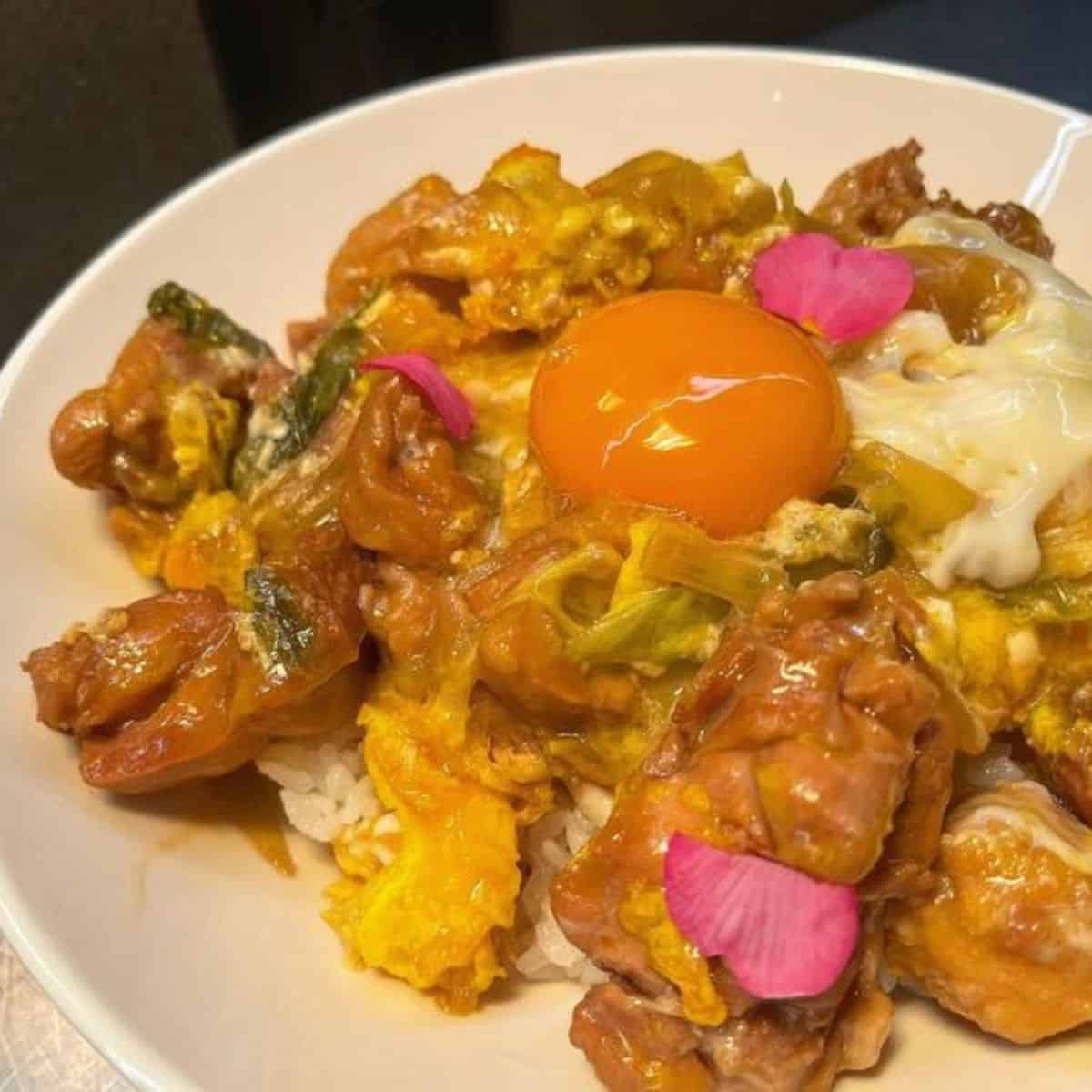 Beautiful Oyakodon plating with fresh egg yolk in the middle and pink flower petals as decor