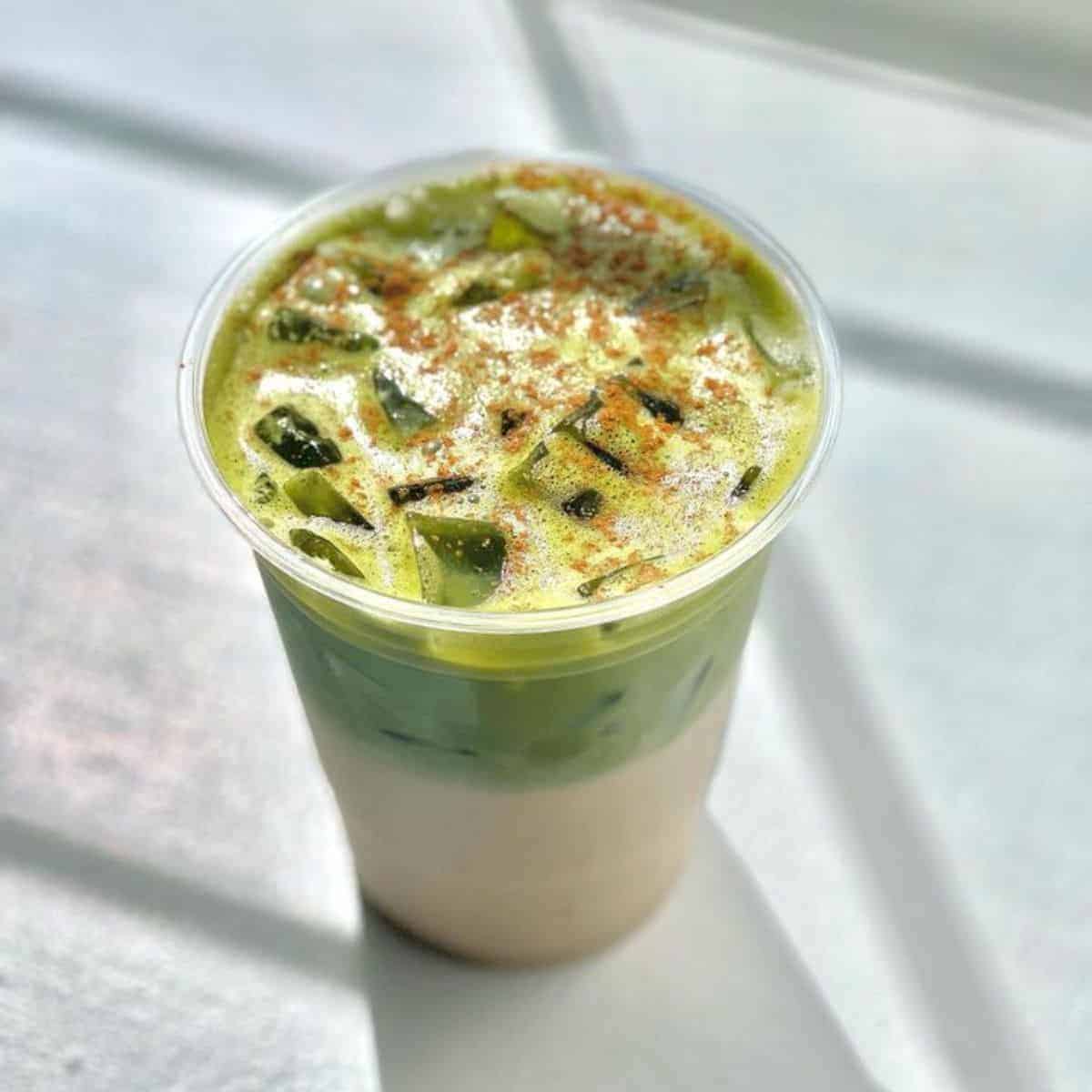 Cold Matcha Chai Latte drink sprinkled with a brown powder in a plastic, transparent cup