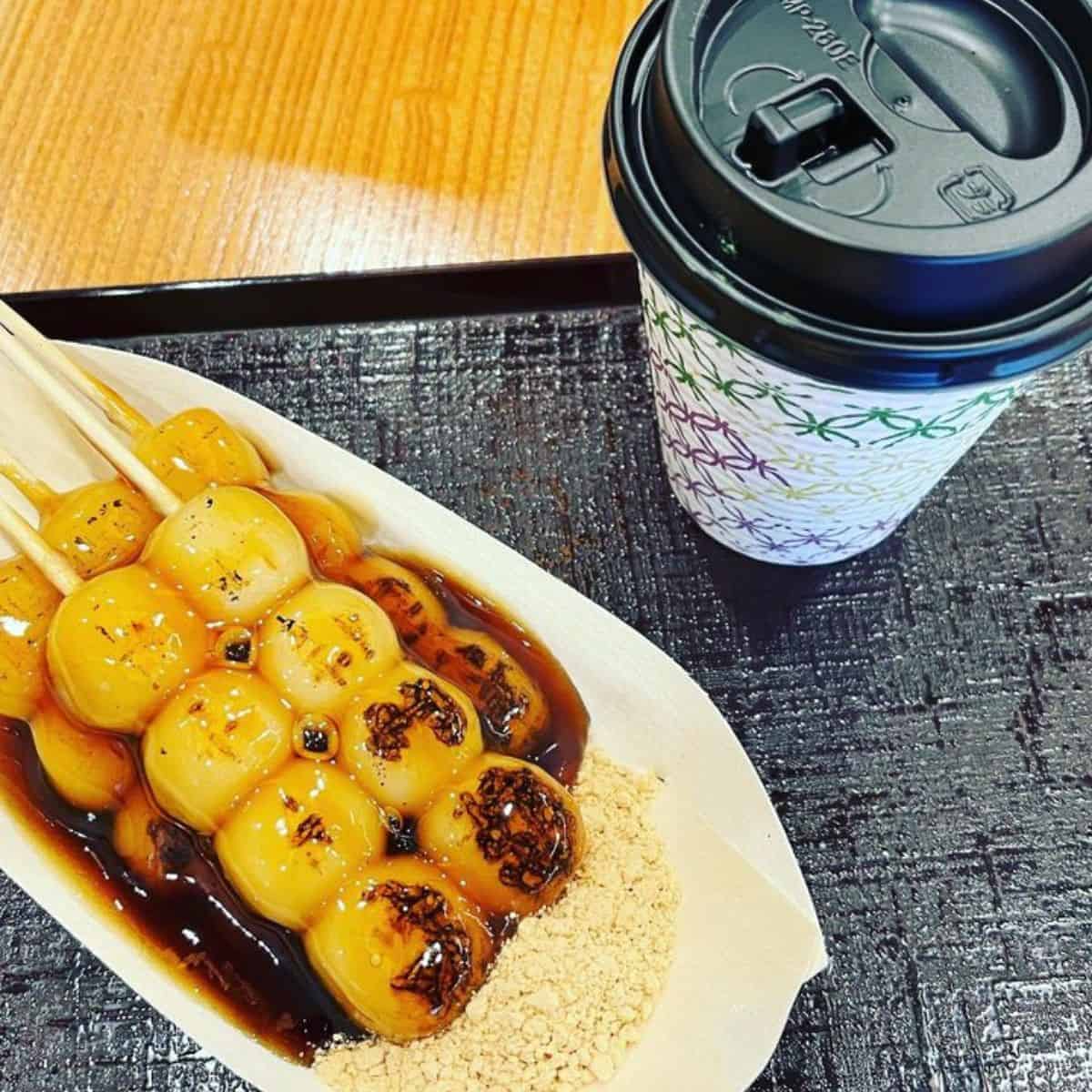 Drizzled skewered rice dumplings in a white plate with white powder on the same plate paired with coffee