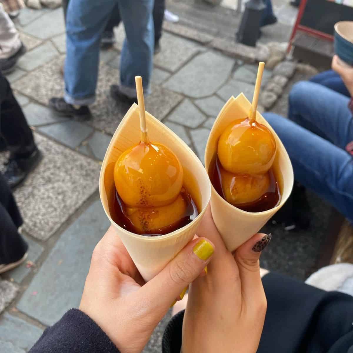 Two girls holding a beautifully wrapped Mitarashi Dango in the busy streets of Japan