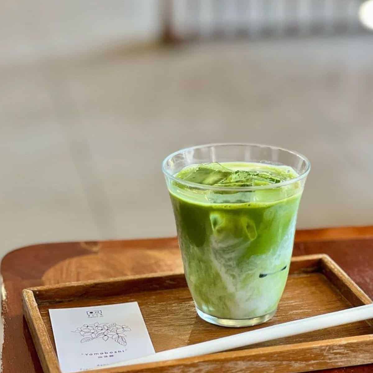 Ice cold glass of Matcha Latte with ice cubes in a woody serving tray