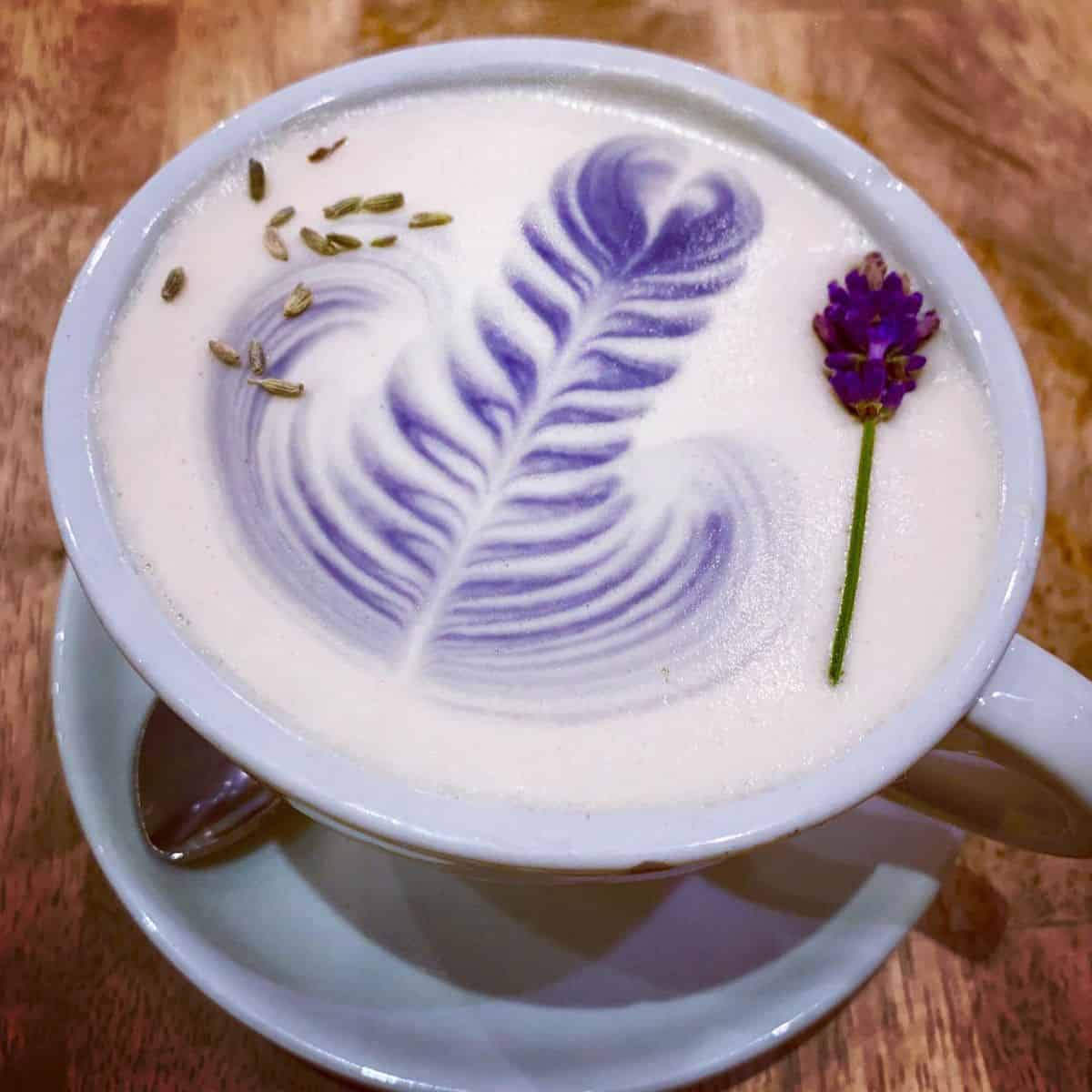 Beautiful cup of Lavender Milk Tea in a brown table with a lavender bud and seeds as garnishes