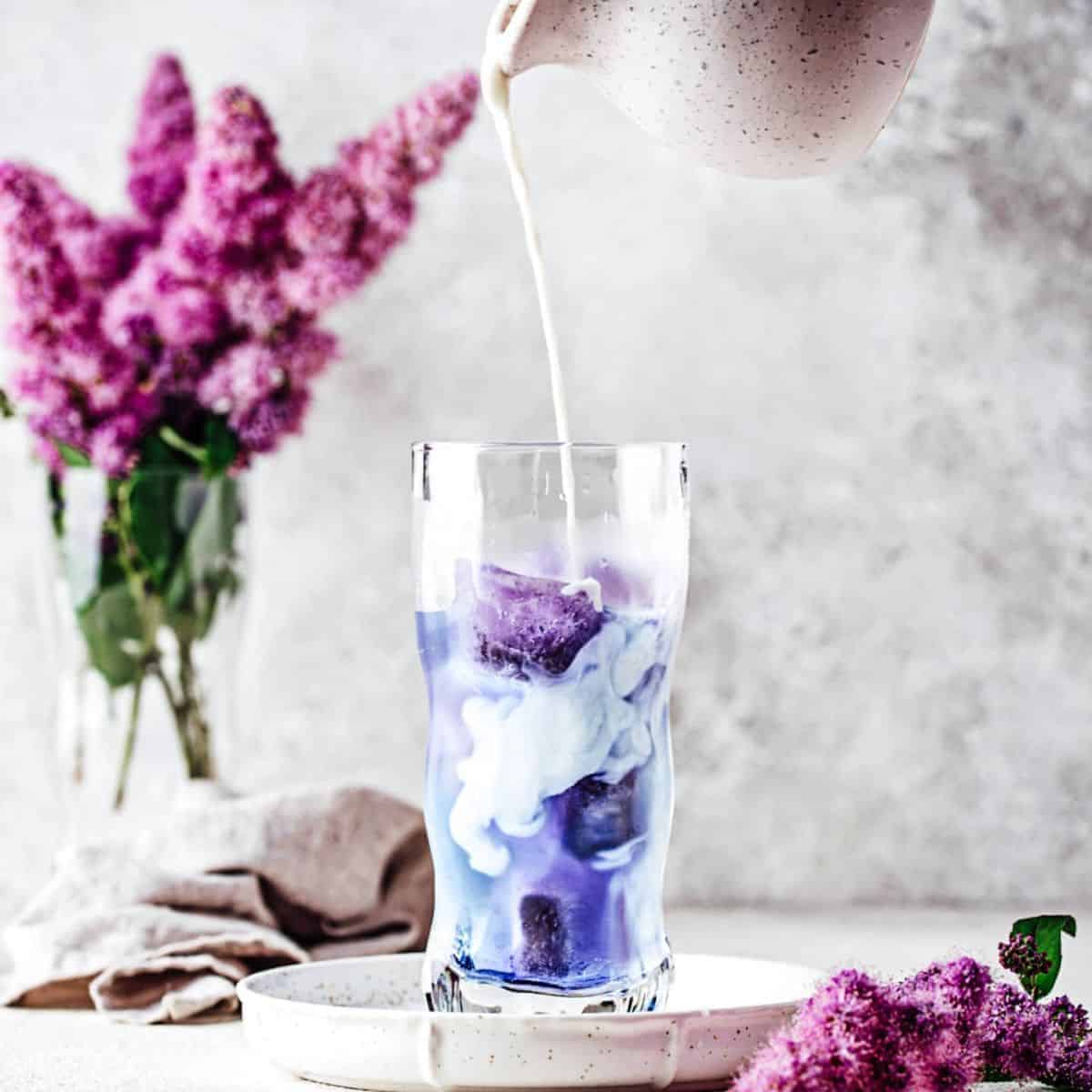 A milk poured in a transparent glass of purplish drink with pink flowers fading on the background