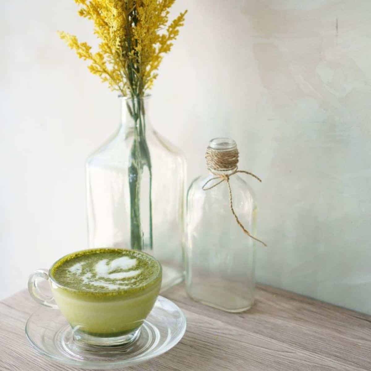 A transparent cup filled with Matcha Latte with yellow flowers in a vase 