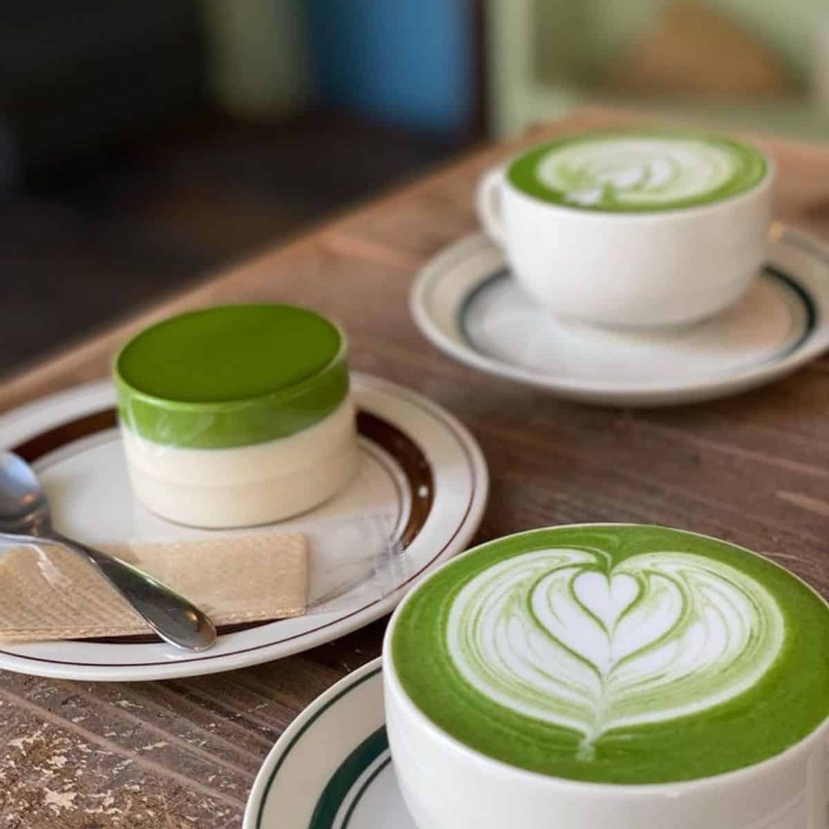 Two delicious cups of Matcha Latte with one serving of pudding in a woody table