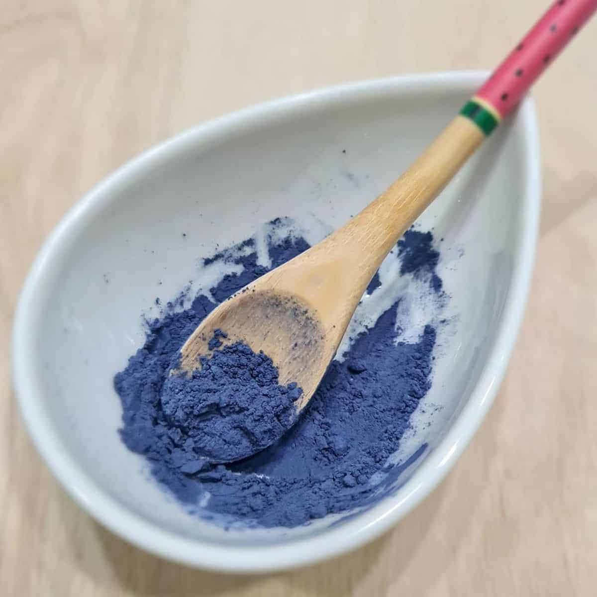 Blue Pea flower powder in a white bowl with a wooden spoon