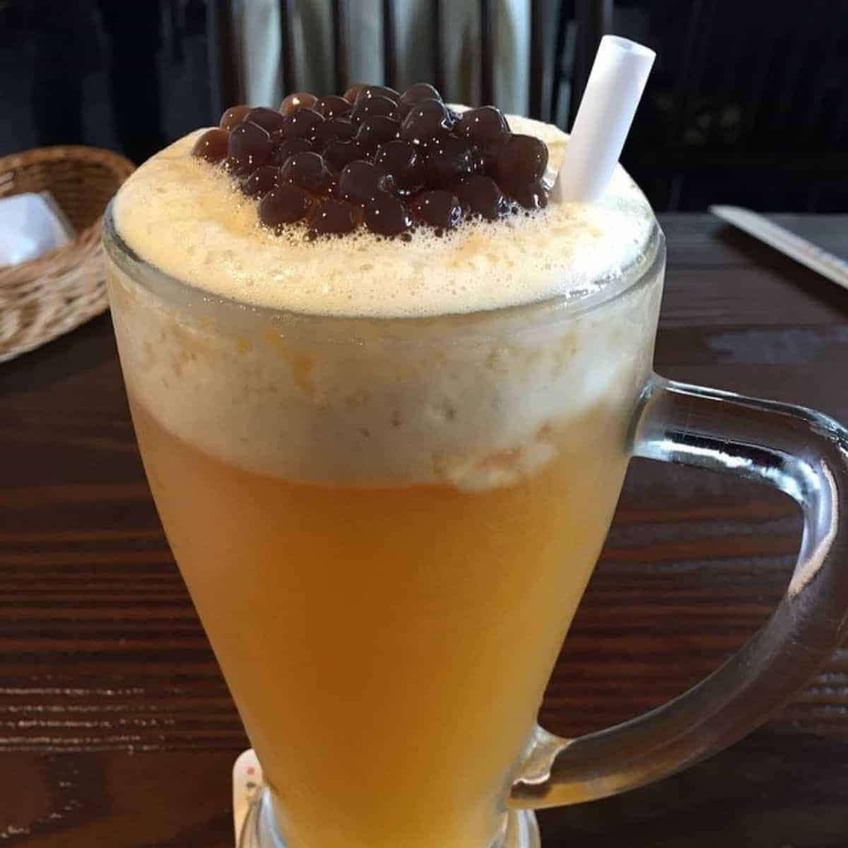  A full glass of fruity beverage with bubbles on top and black tapioca pearls.