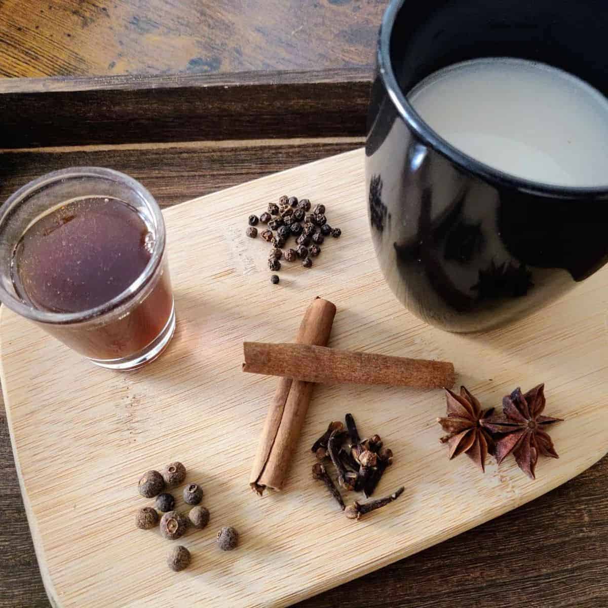 Chai syrup in dark brown colour, cashew milk and spices in a wooden tray