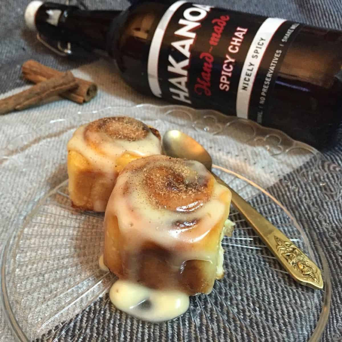 Cinnamon rolls glazed with chai syrup and a bottle of spicy chai in the background.
