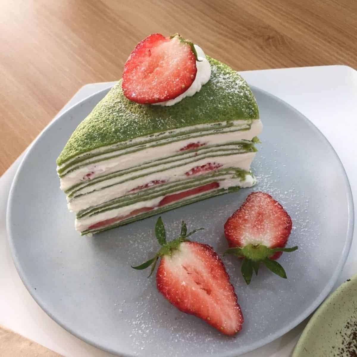 Beautiful reddish fruity fillings of a green tea crepe cake and three slices of fresh strawberries