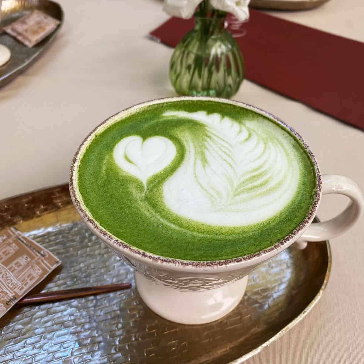 A hot cup of green beverage with art on top