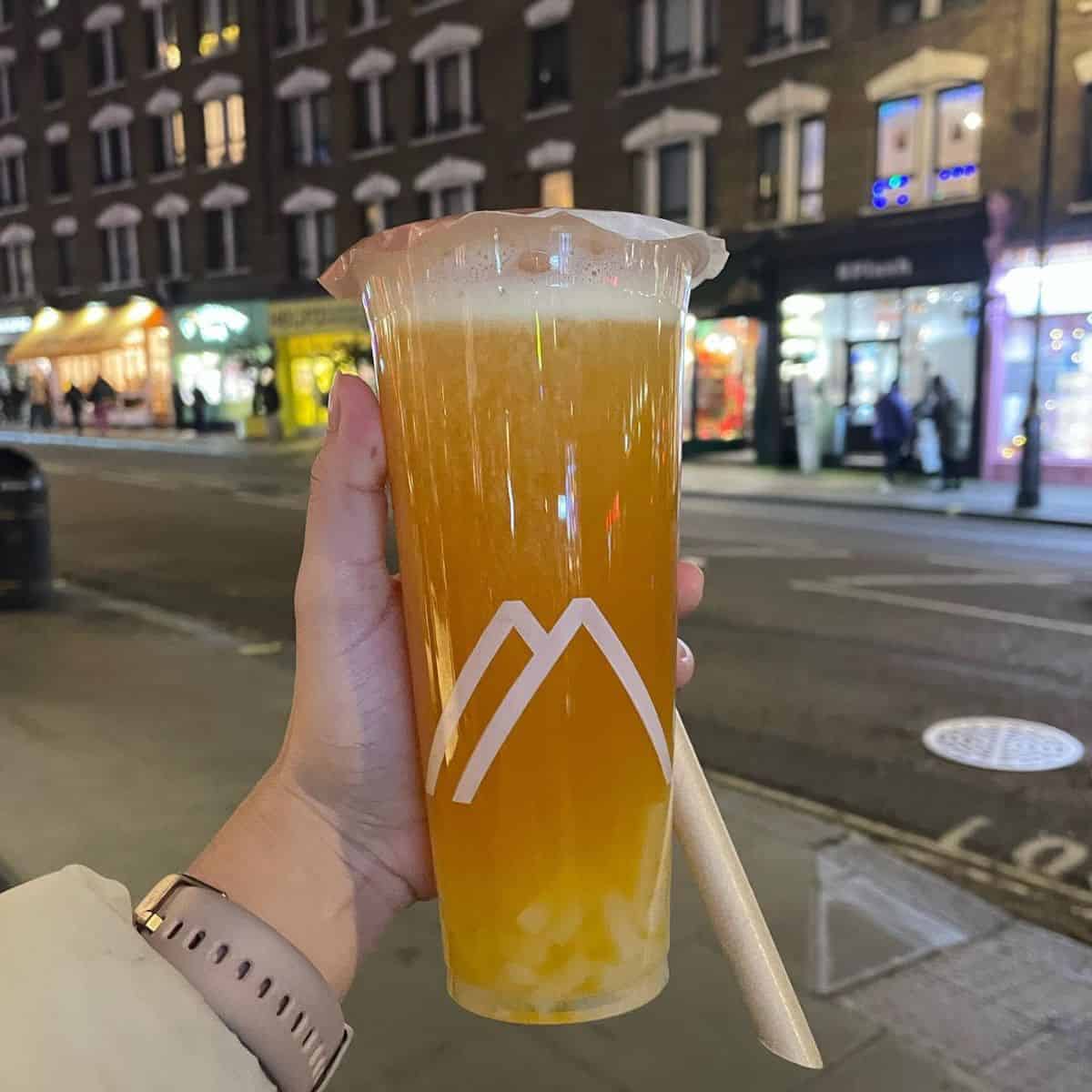 A lady holding Passion Fruit Boba  while strolling in the streets at night