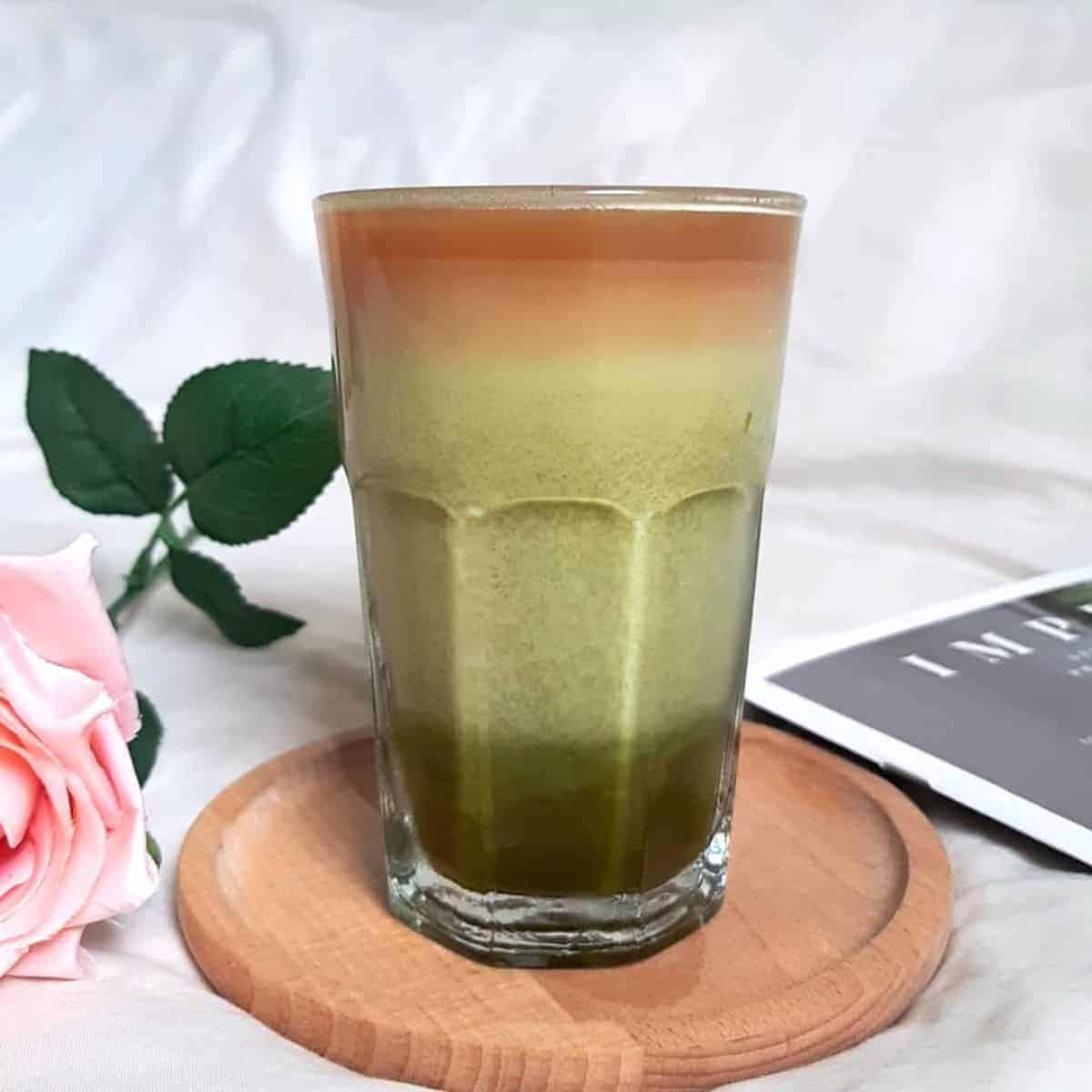 Matcha coffee with beautiful layers on top of a wooden coaster with pink rose on the side