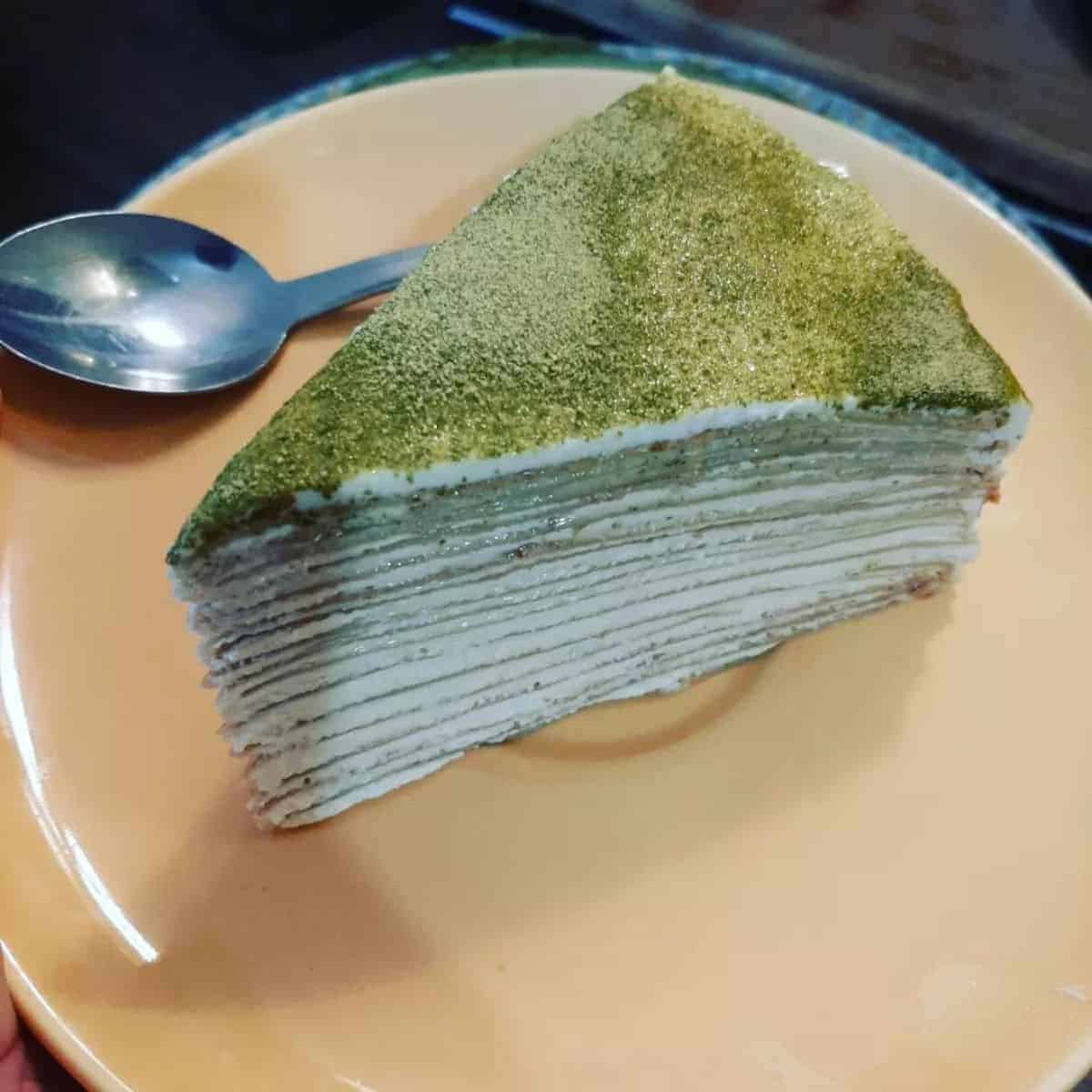 Mouth-melting Matcha Crepe Cake slice in a peach plate with a spoon on the side