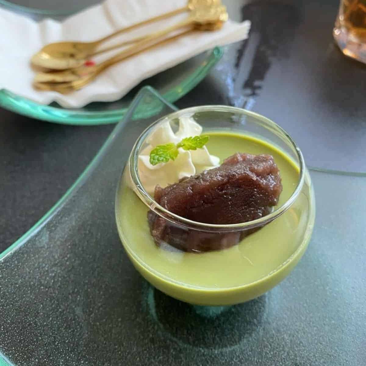 A delicious serving of Matcha Pudding with red bean paste and whipped cream in a transparent glass