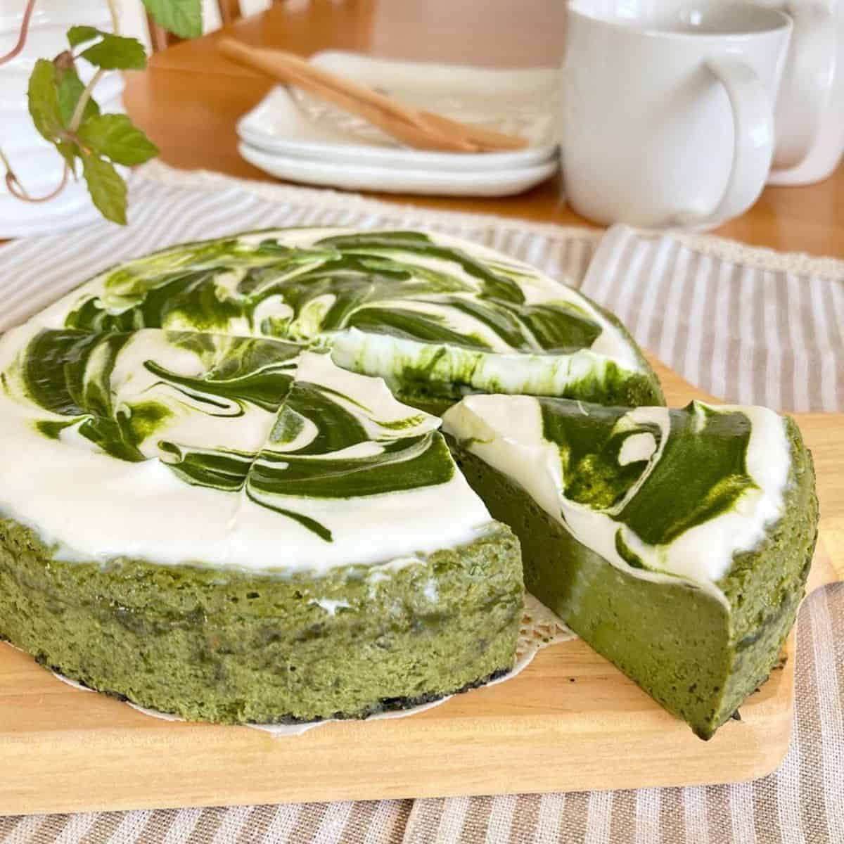 Matcha cheesecake on a woody board with white utensils in the background