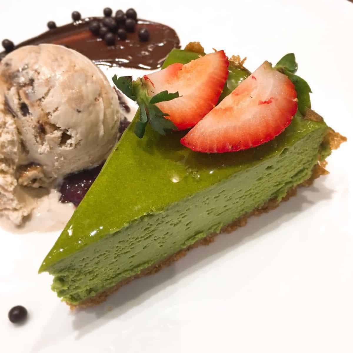 One slice of a green dessert with slices of fresh strawberries on top paired with ice cream