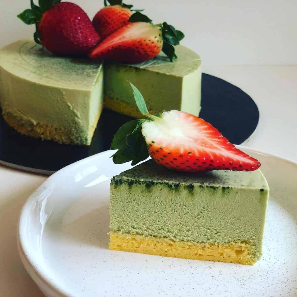 One layer of Matcha cheesecake in a black tray and one cake slice in a white plate with fresh strawberry slices