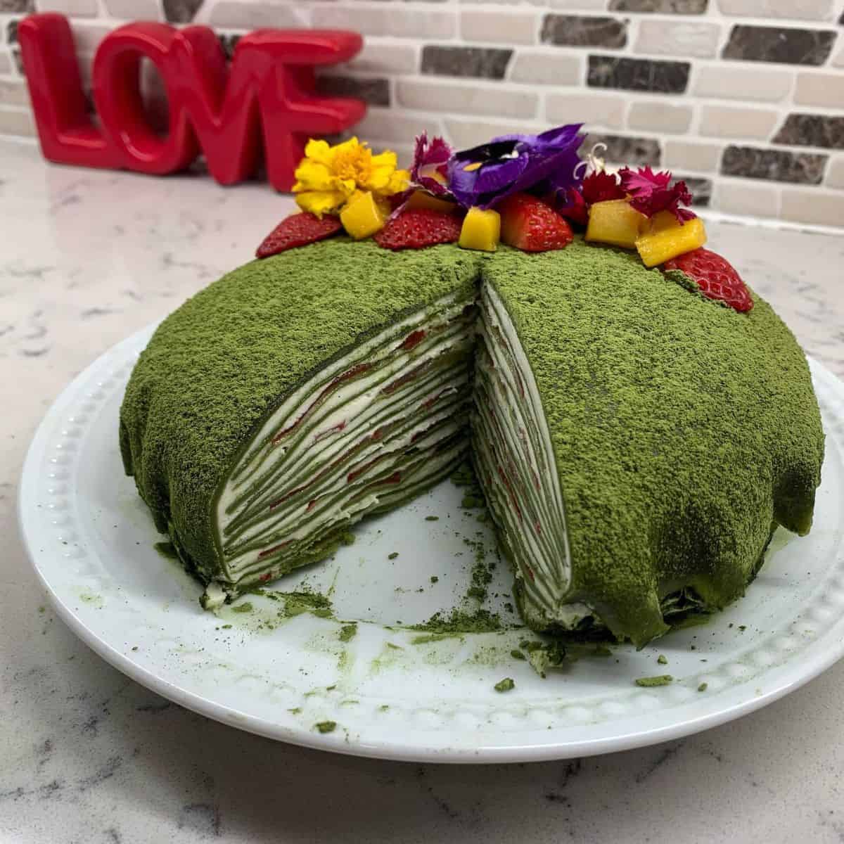 A Matcha Crepe Cake topped with fresh strawberries and edible flowers