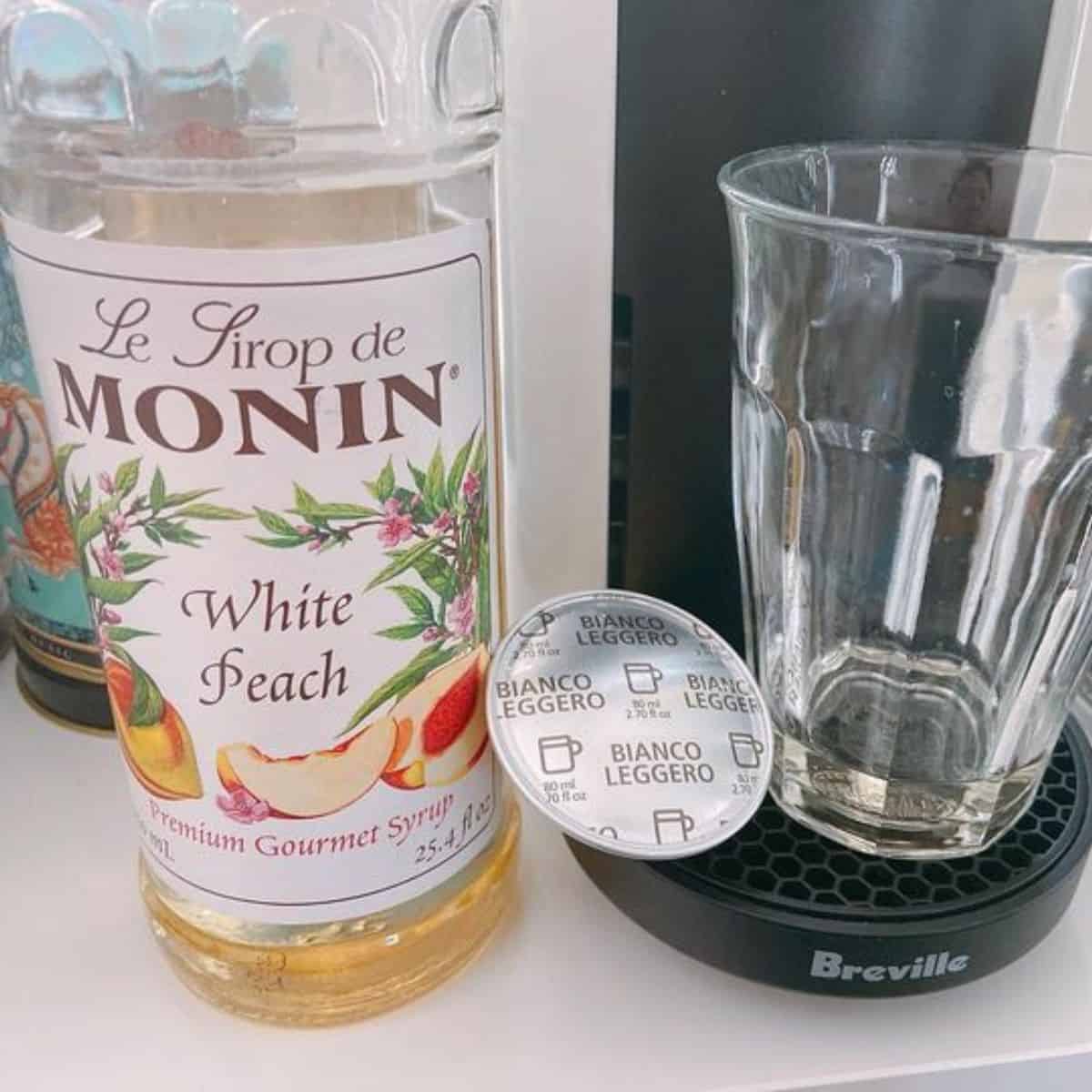 A transparent bottle of Monin white peach syrup and an empty glass