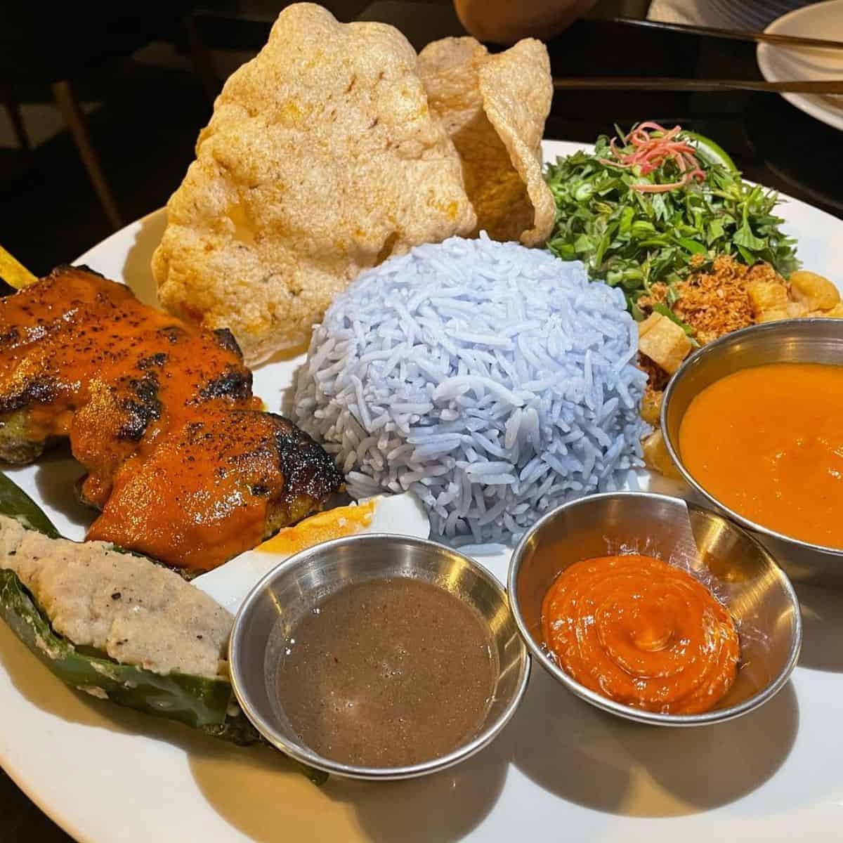 Delicious Nasi Kerabu with grilled meat, salad, and three different sauces