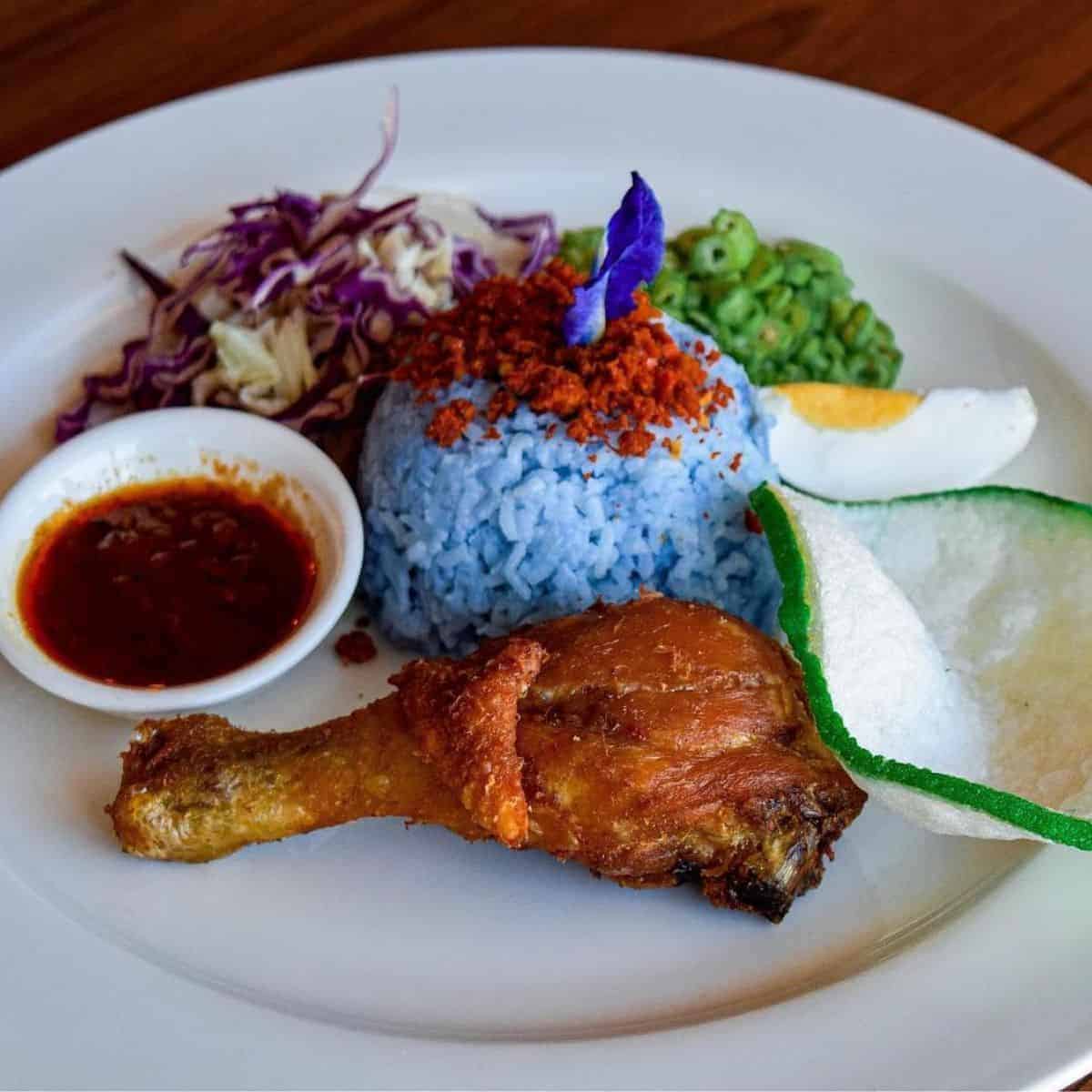 One full meal of Nasi Kerabu with fried chicken served on a white plate