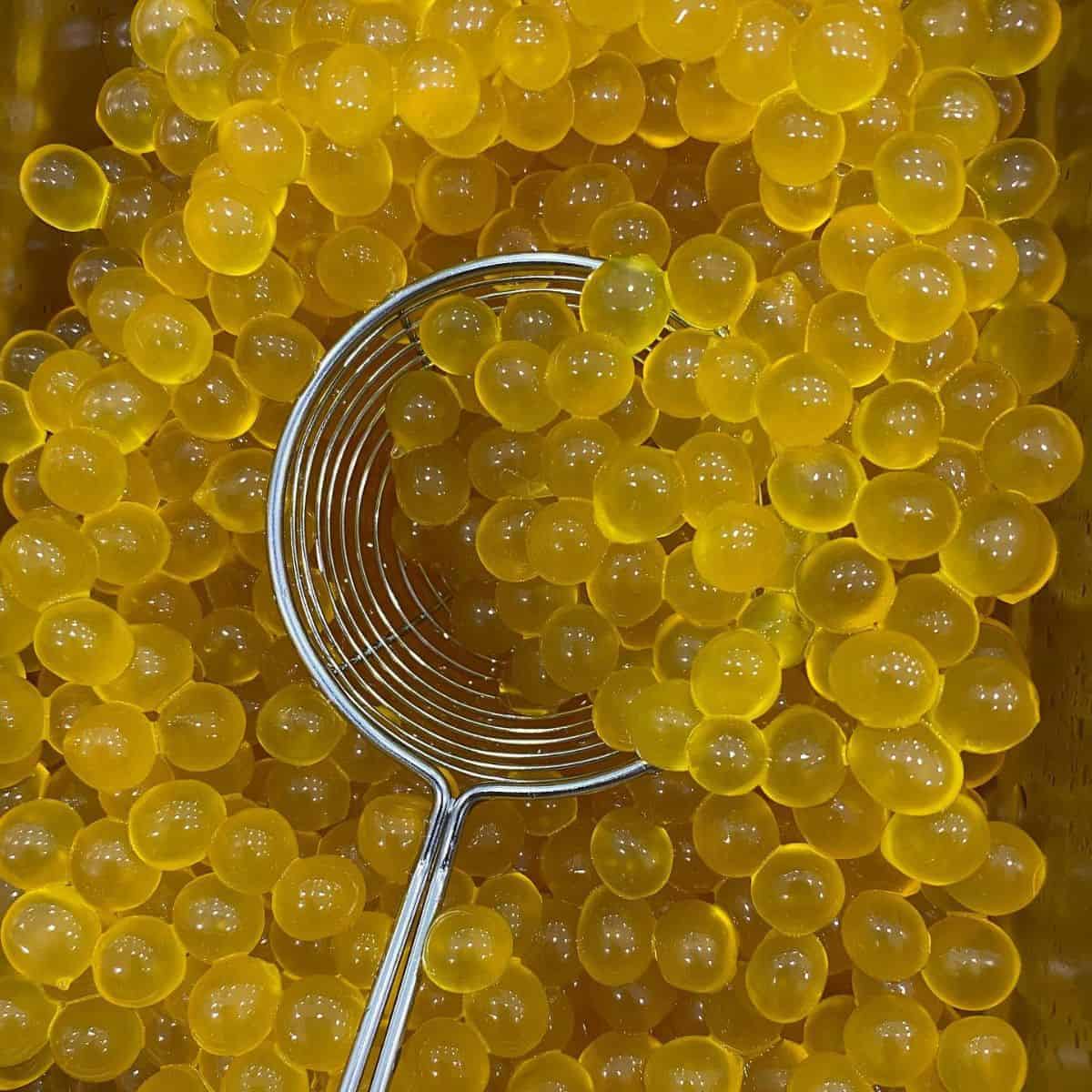Chewy tapioca  pearls in yellow colour with a silver strainer.