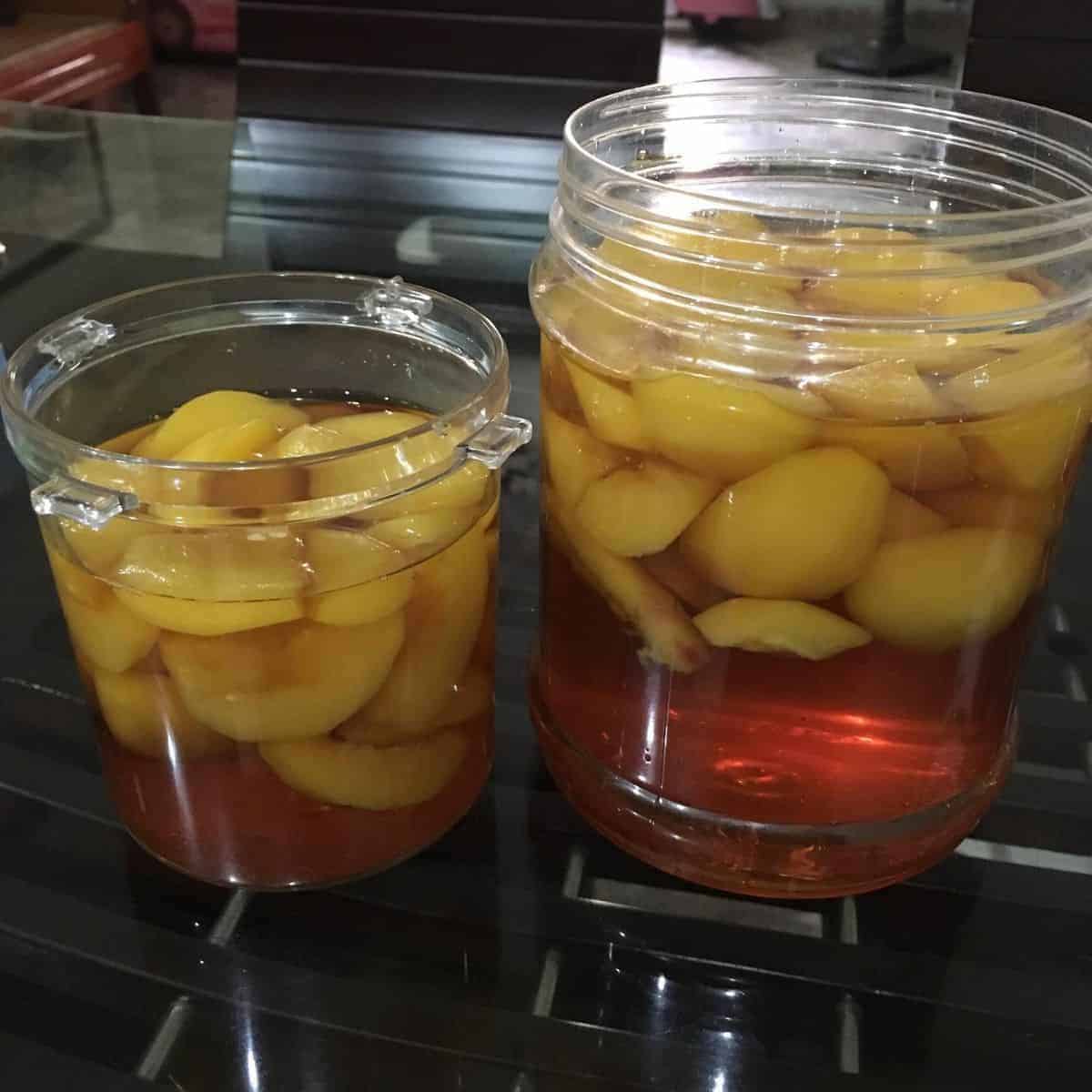  Peach syrup in two large storages with chunks of peaches