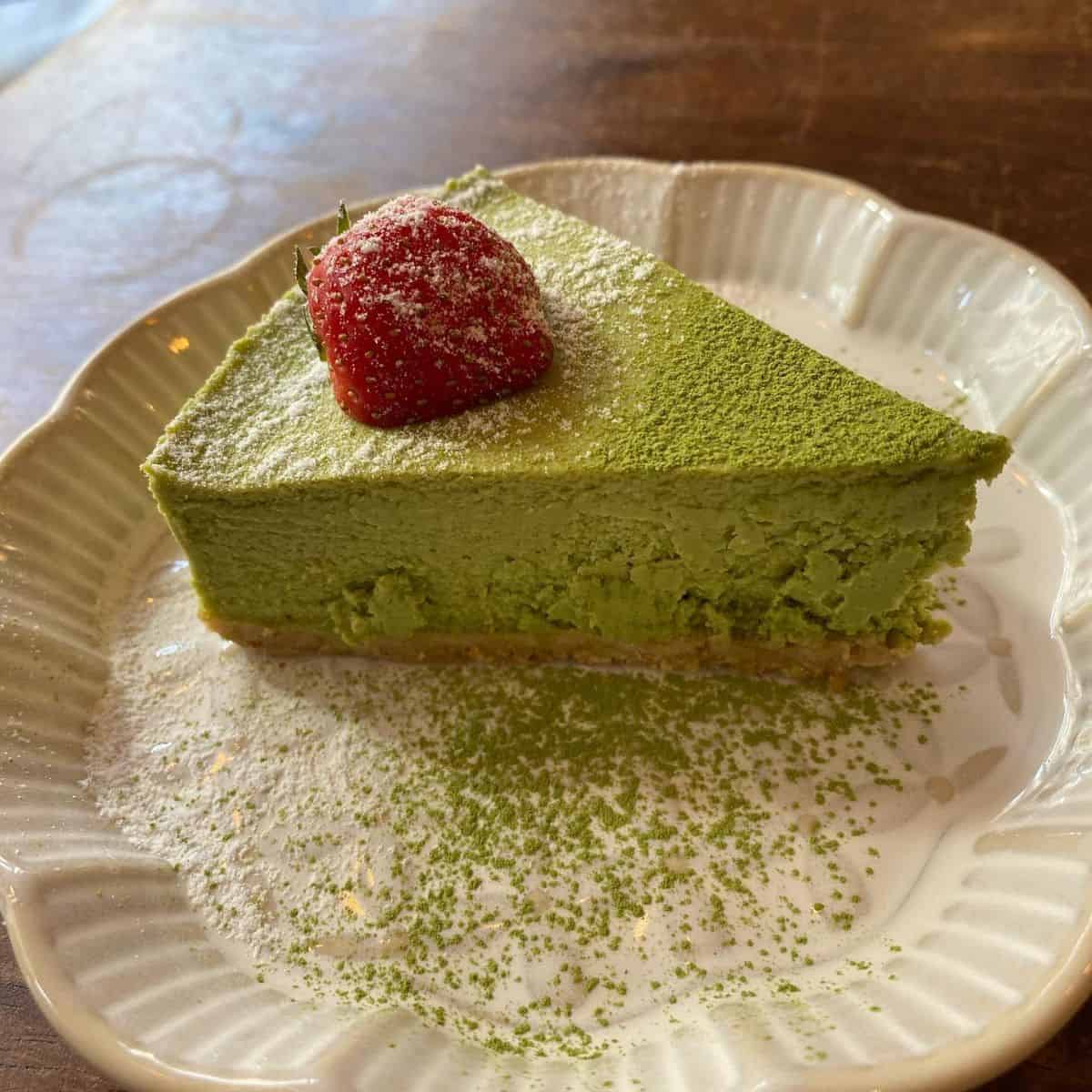 A slice of green tea dessert topped with fresh strawberry on a white ceramic plate