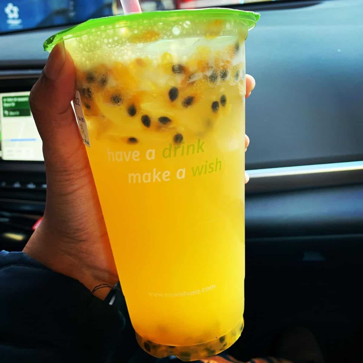 A full glass of Passion Fruit Boba with fresh fruit seeds held by one hand inside a car