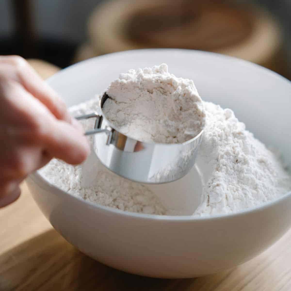 A hand scooping a tapioca flour from a white bowl