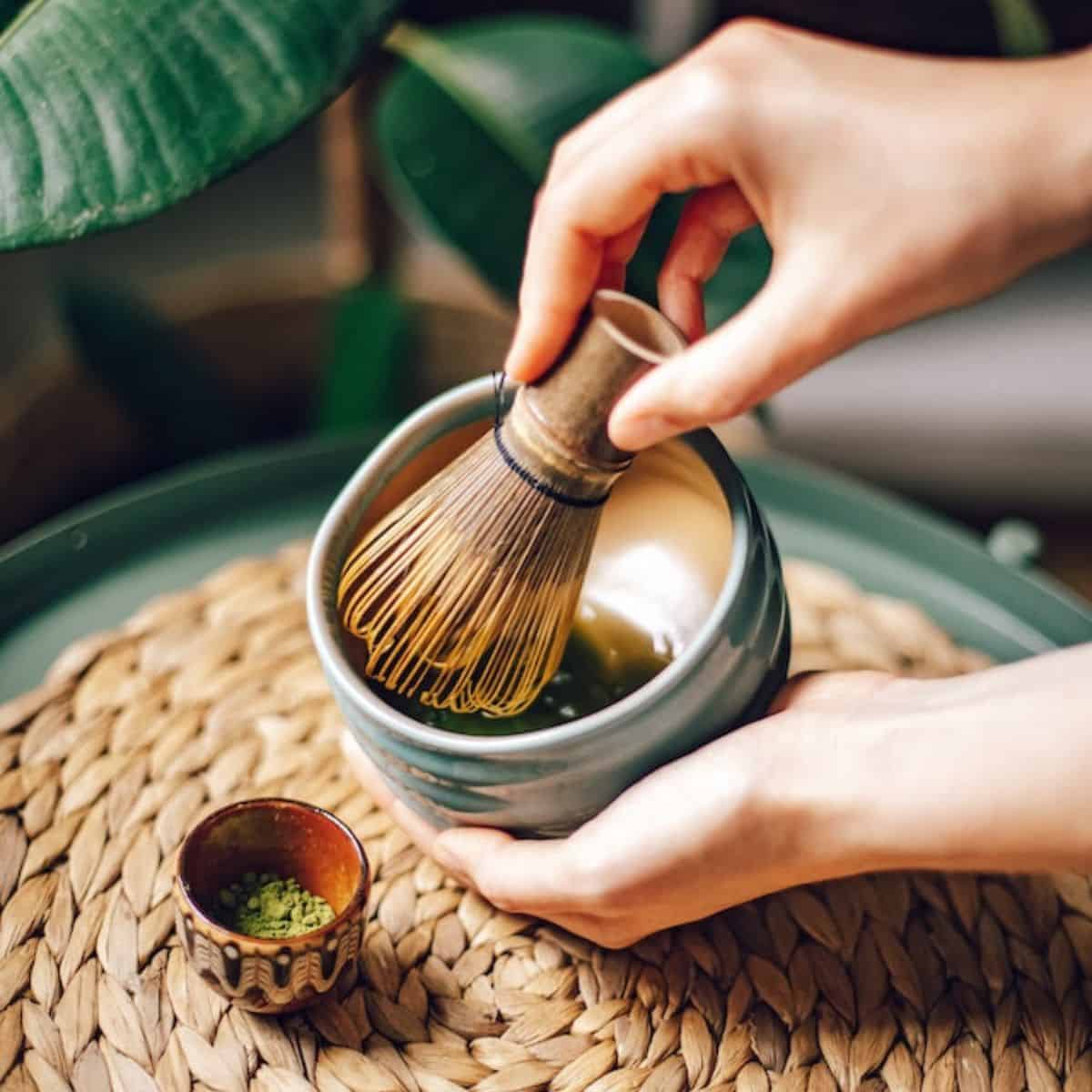 A person whisking the green tea using a bamboo whisk