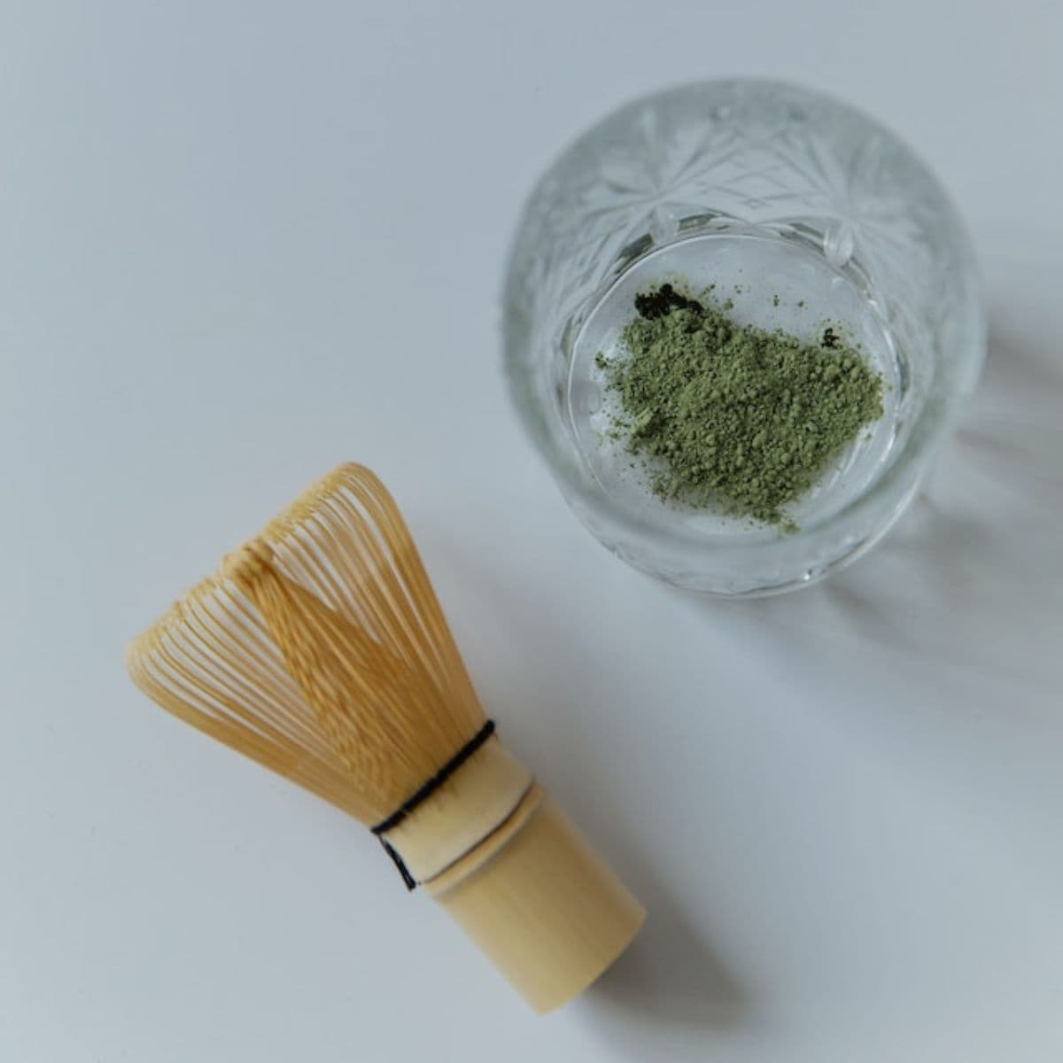 Transparent glass with matcha powder and a bamboo whisk
