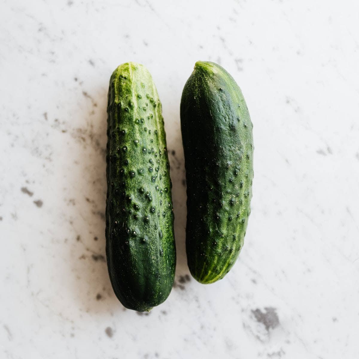 Two elongated green vegetables on a marbled table